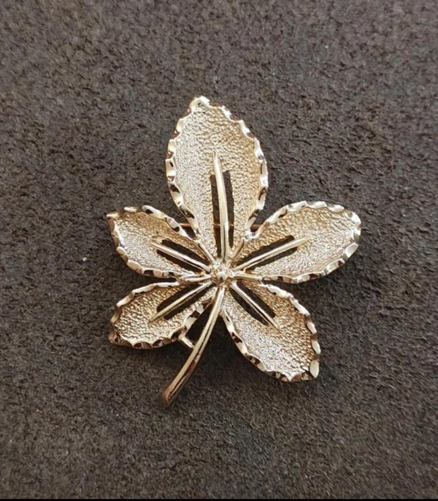 Gold-tone leaf flower brooch on dark background; five petals with central stem