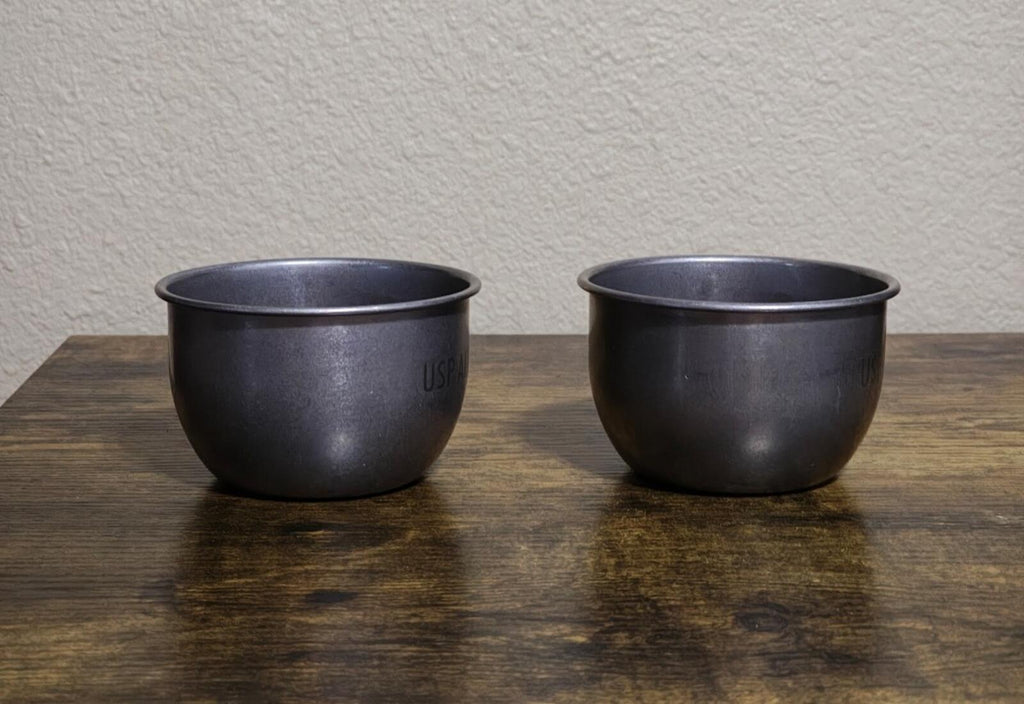 Two dark stainless steel mugs with handles, minimal front markings visible