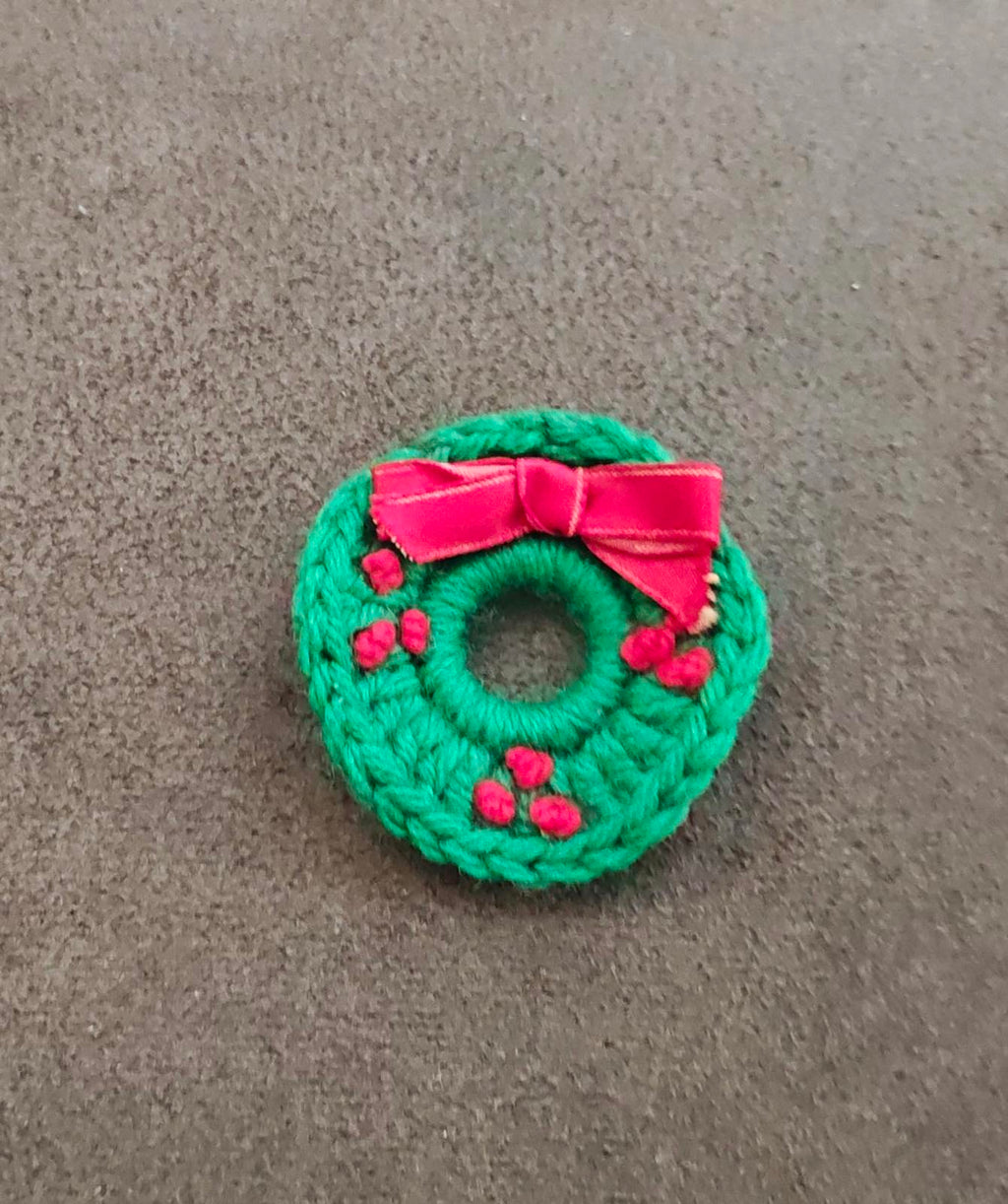 Green knitted wreath brooch with pink bow and red berry details, small round knit front
