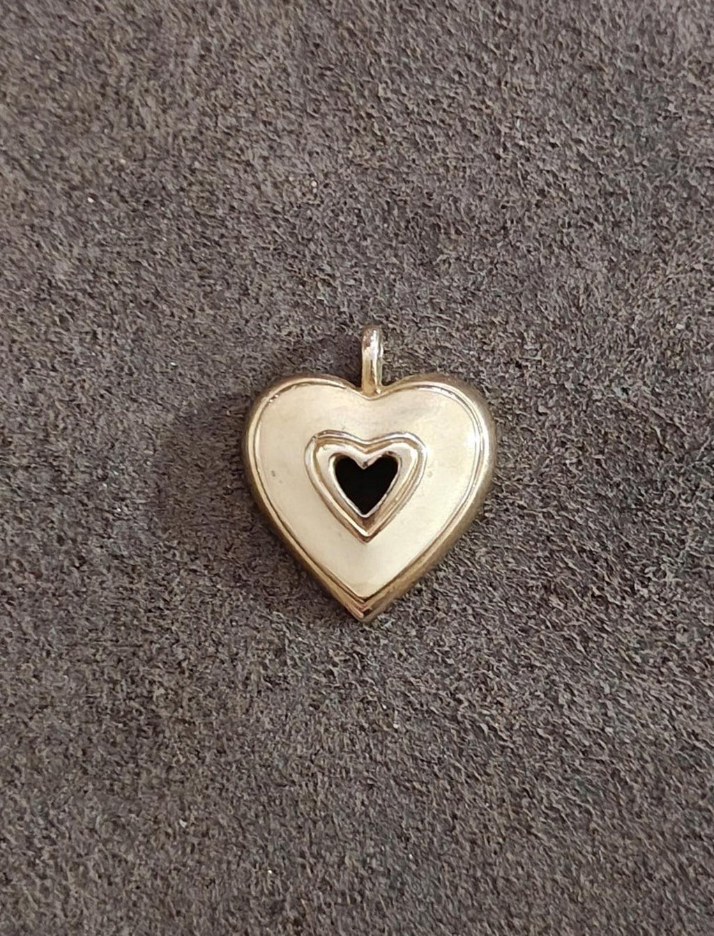 Gold tone heart pendant with white enamel face and black heart center, centered on dark fabric
