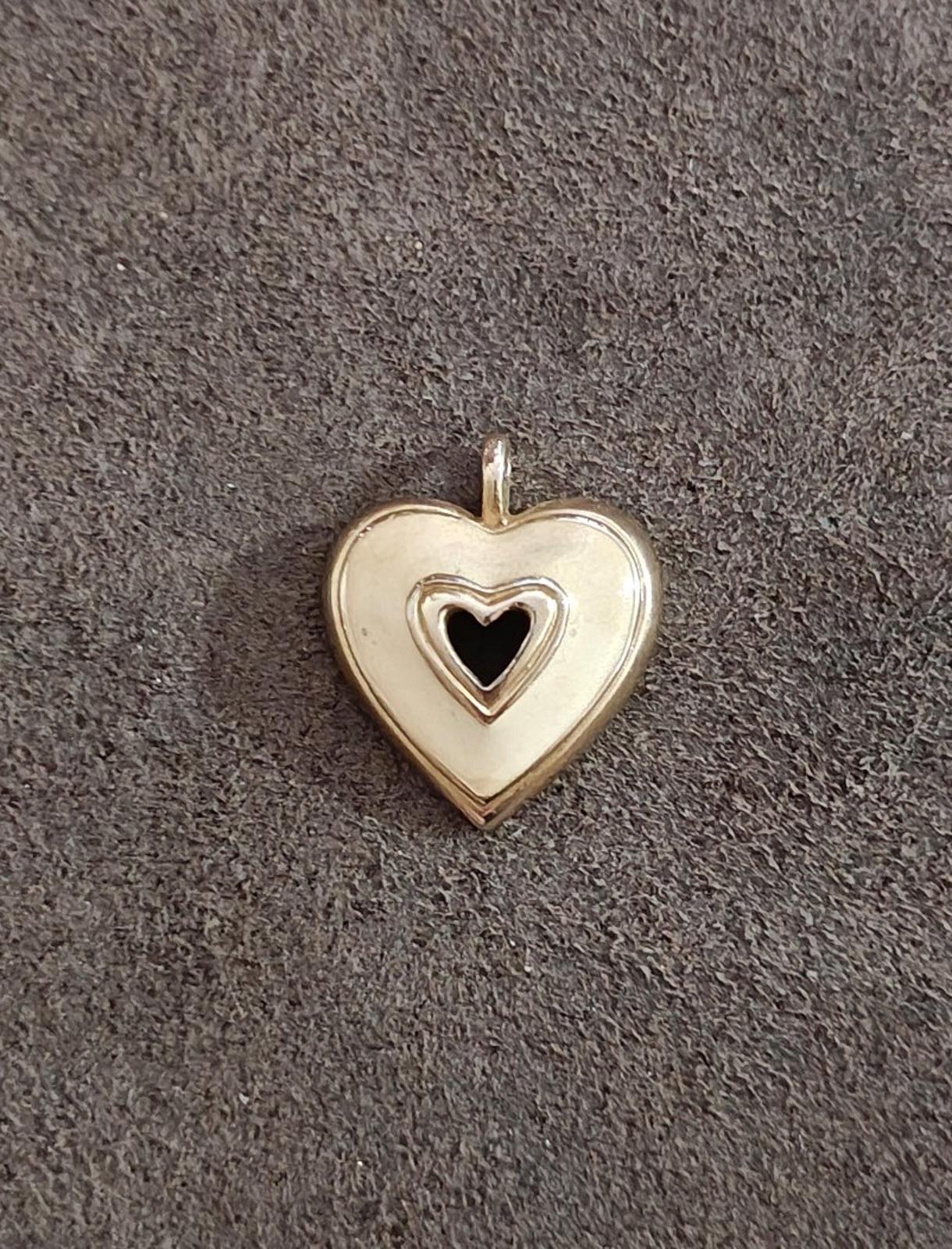 Gold tone heart pendant with white enamel face and black heart center, centered on dark fabric