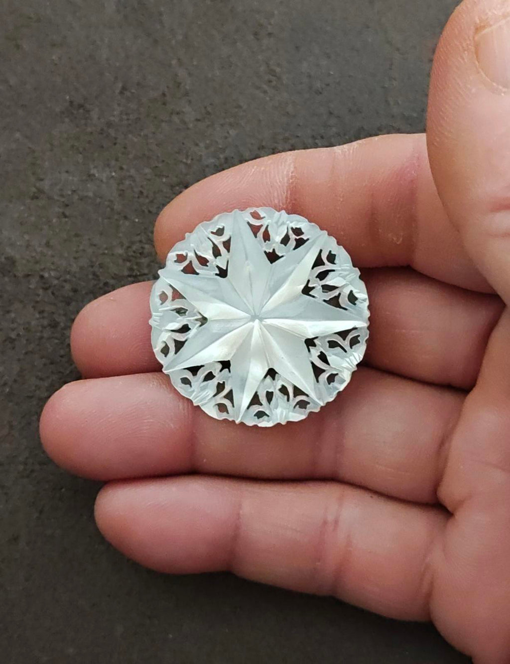 White mother-of-pearl Star of Bethlehem brooch, carved round starburst held in hand