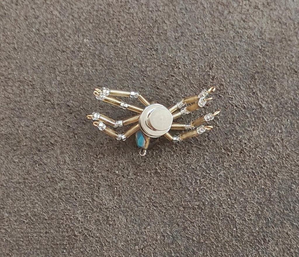 Silver-toned beaded spider pin with crystal bead legs and round metal center.