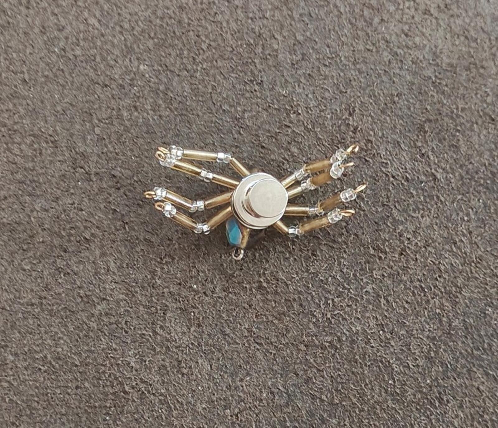 Silver-toned beaded spider pin with crystal bead legs and round metal center.