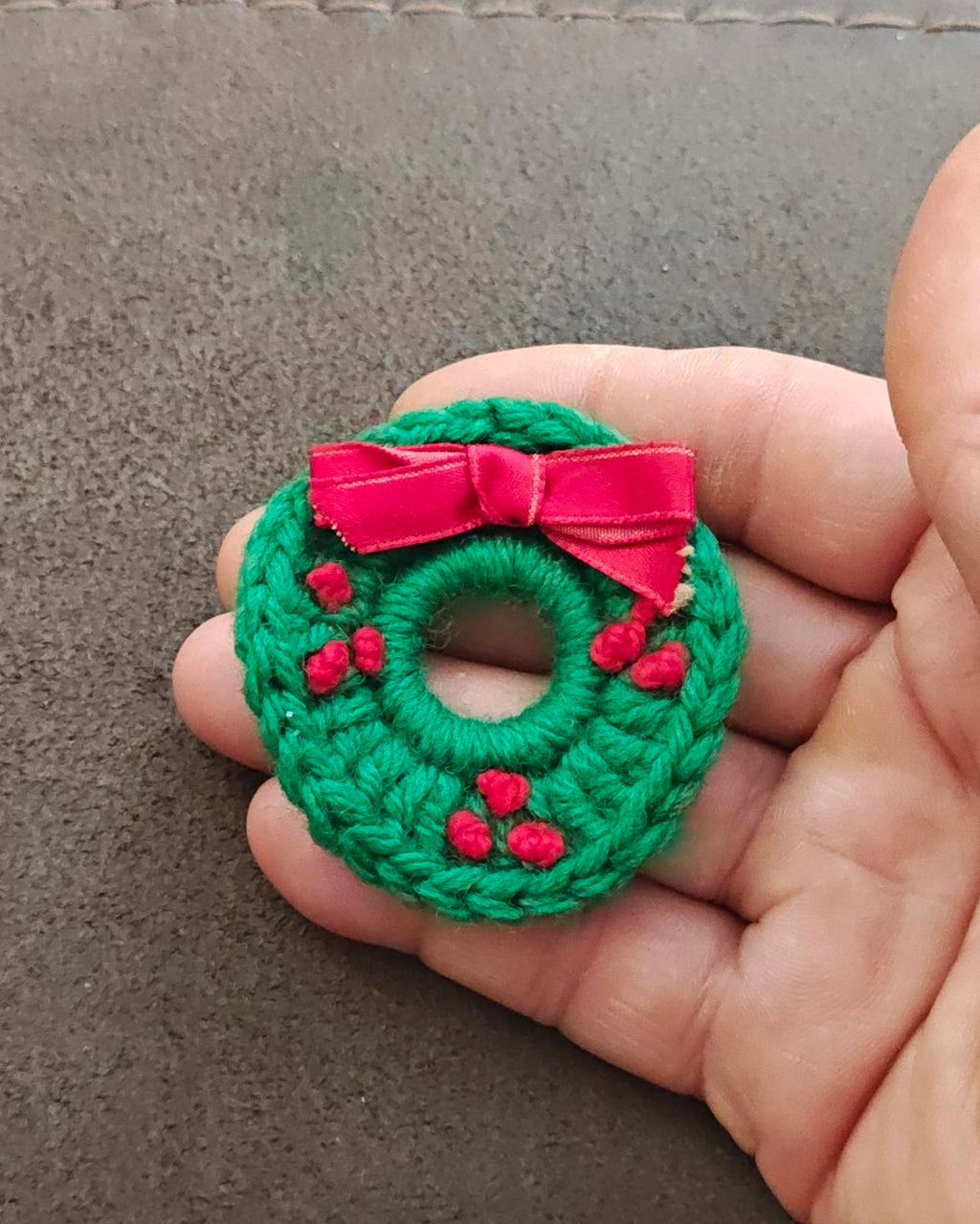 Green knitted wreath brooch with pink bow and red berries, close-up in hand