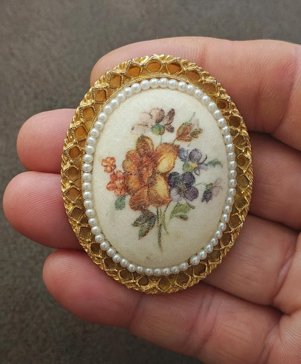 Gold oval ceramic floral brooch close-up with faux pearls around ornate gold bezel