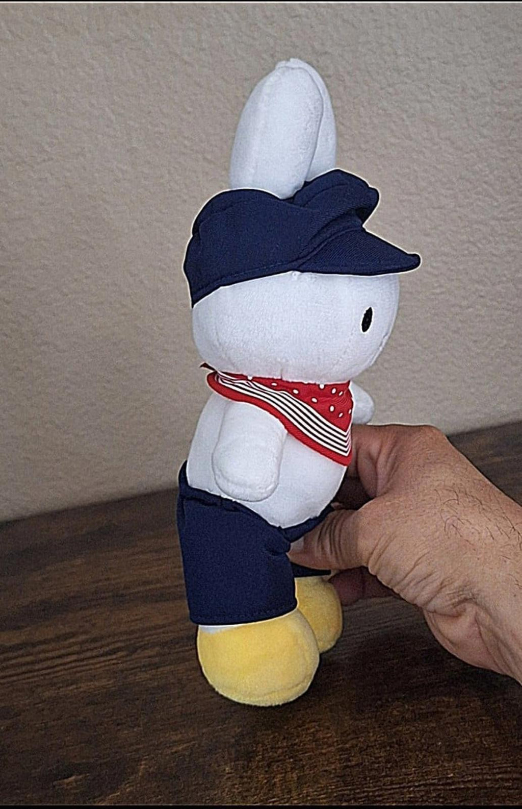 White bunny rabbit plush in profile, navy cap and outfit with red bandana and yellow shoes.