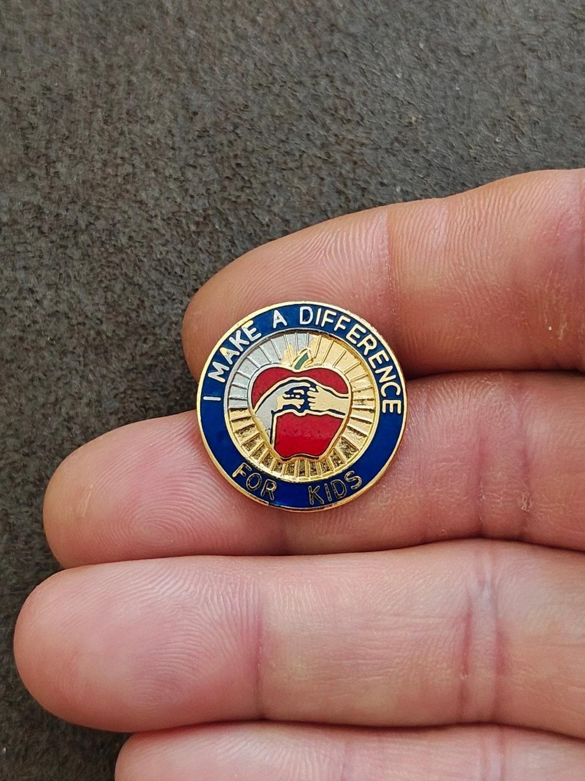 Blue and gold enamel “Make a Difference for Kids” pin with apple and hand details.