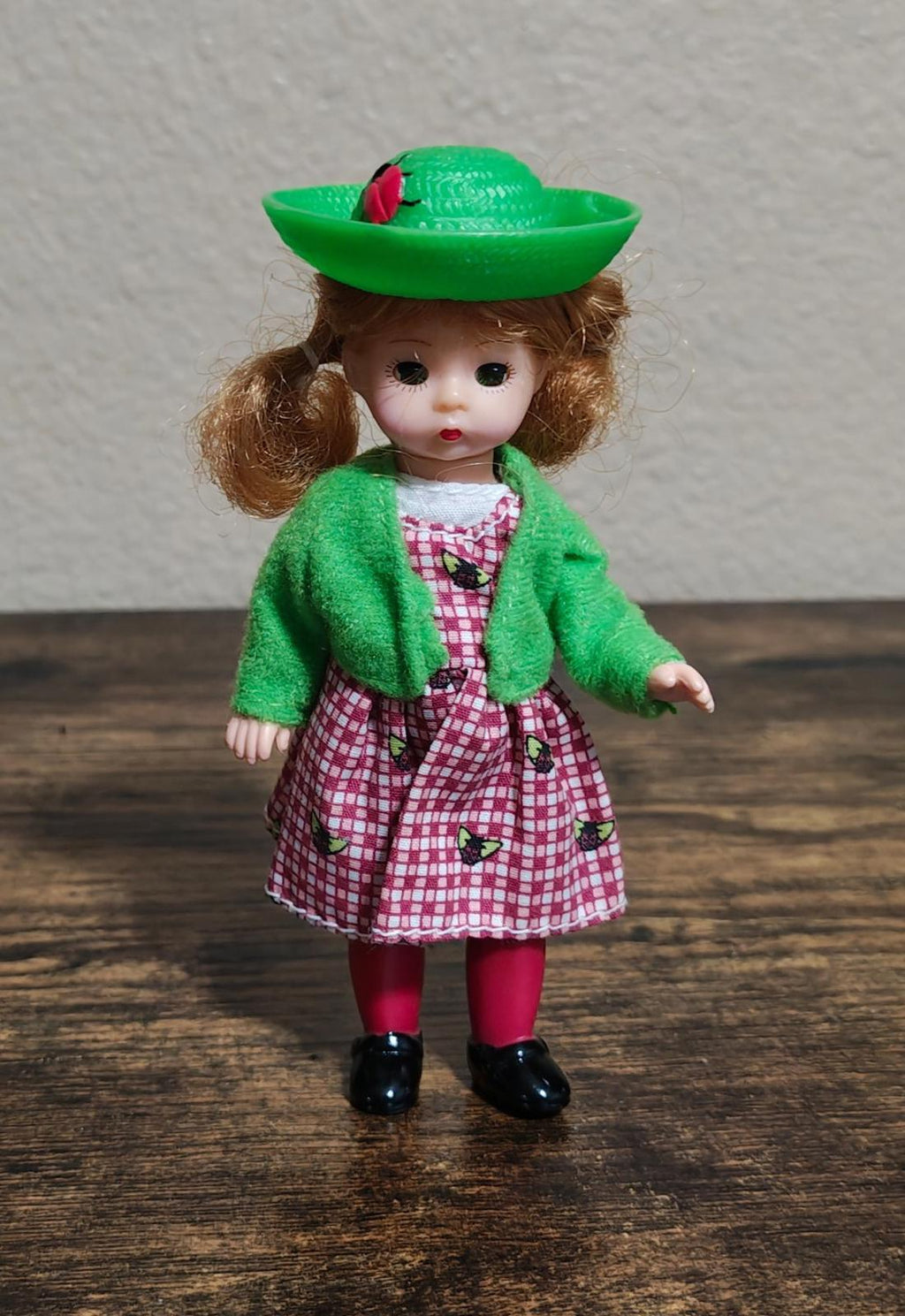 Full-body vintage girl doll standing upright in green hat, green jacket, pink check dress.