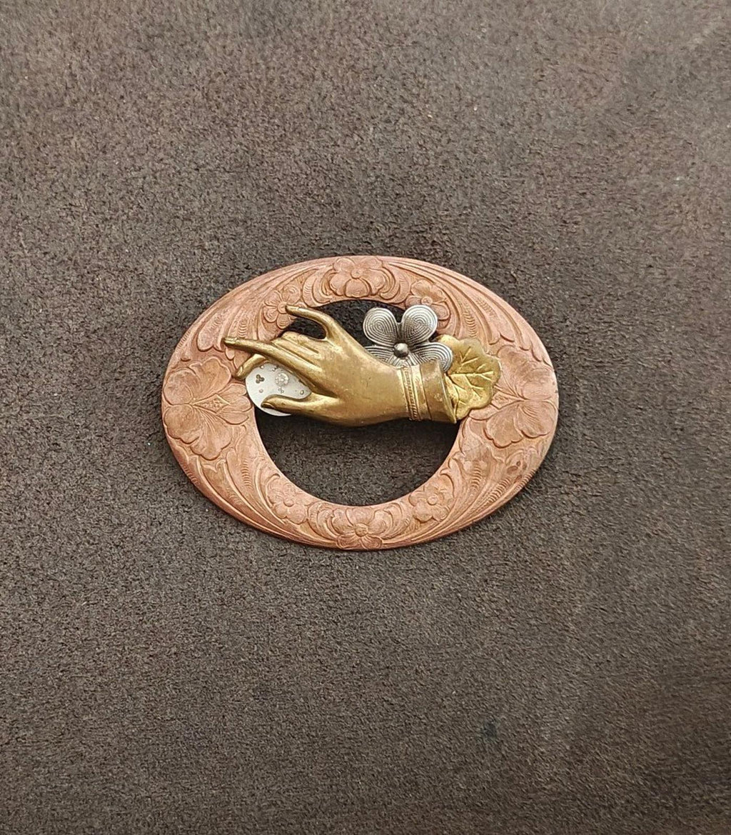 Round engraved bronze-toned brooch featuring a gold bird and gray floral centerpiece