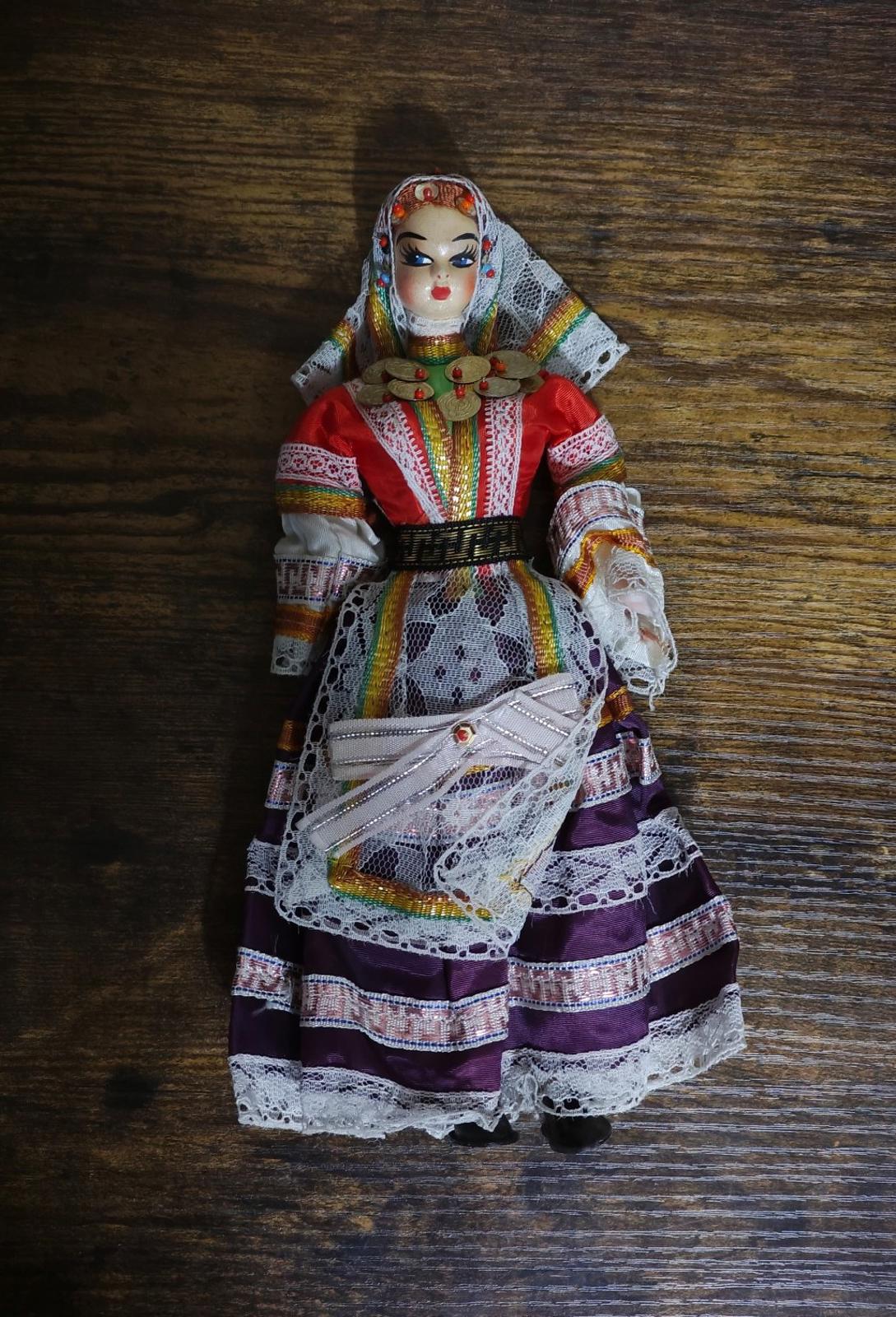 Female folk doll standing in red bodice and purple skirt with lace apron and gold accents