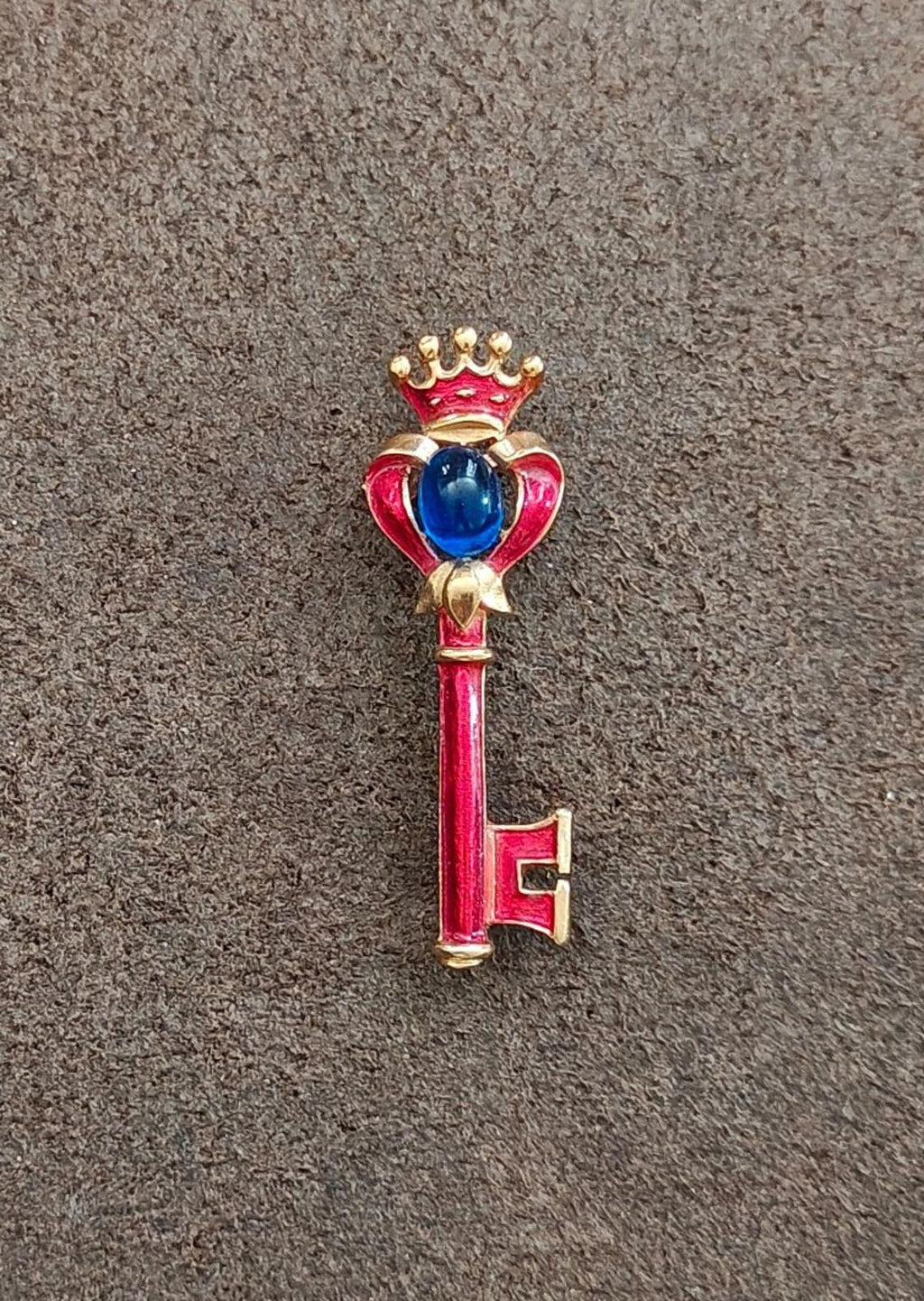 Gold-tone key brooch with red enamel and blue cabochon, crown and heart frame