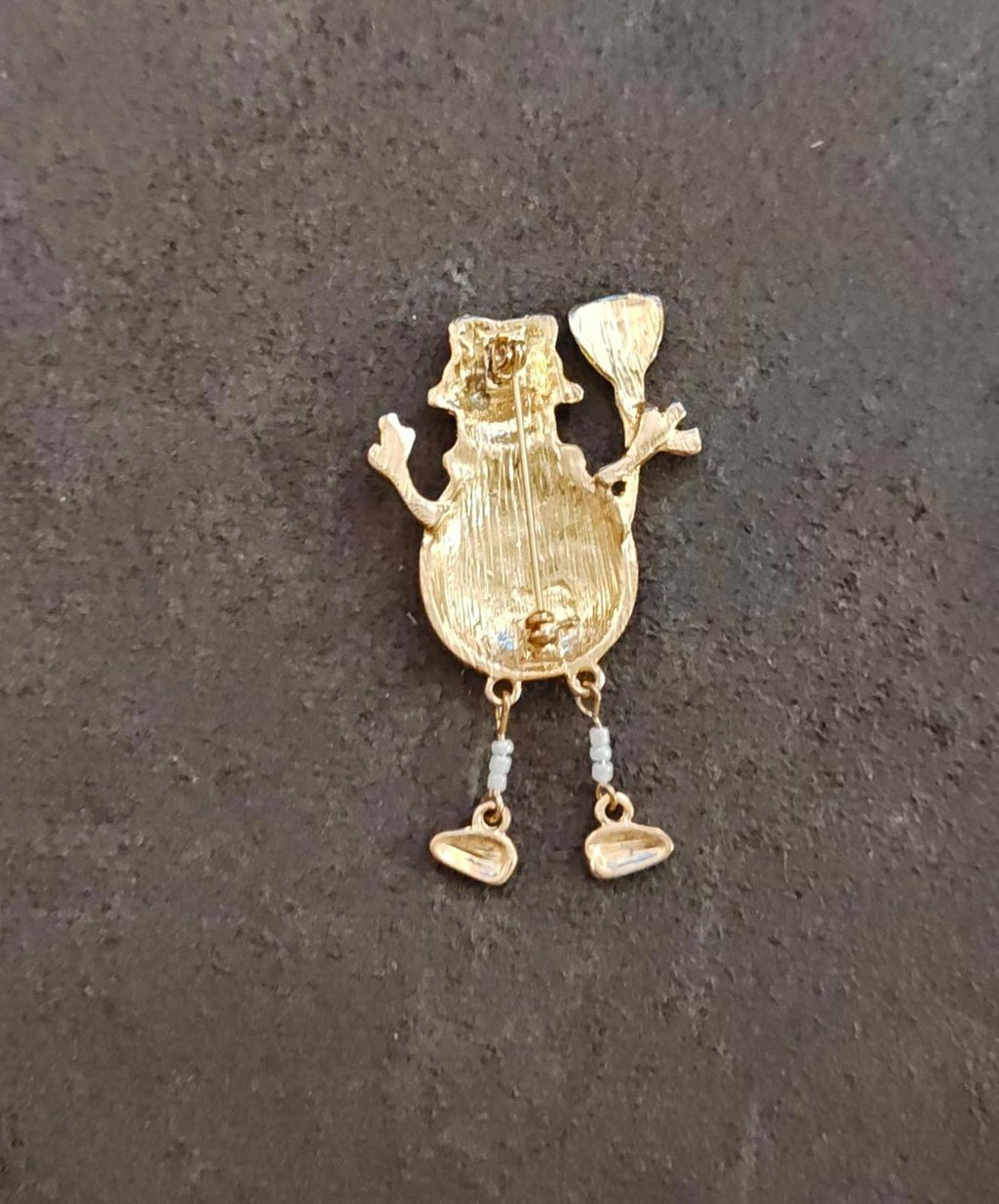 Gold tone back of a snowman enamel brooch with two-pin construction and dangling loops.