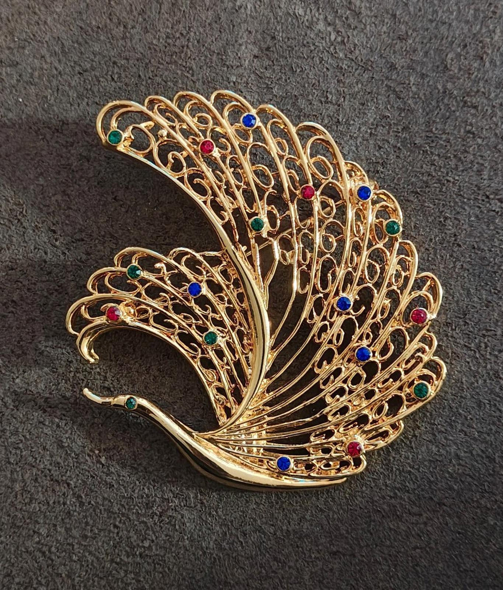 Gold-tone peacock feather brooch pin with red, blue, green crystal spots, angled.