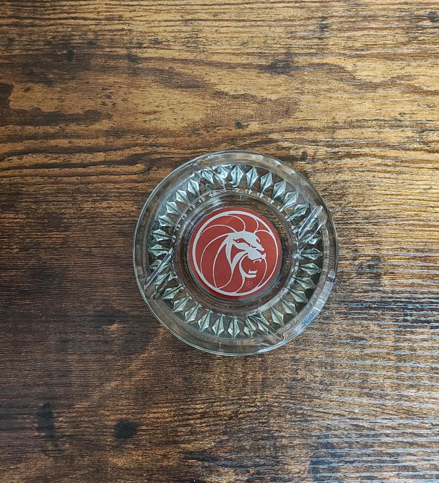 Small clear glass ashtray with red circular emblem and diamond-cut rim