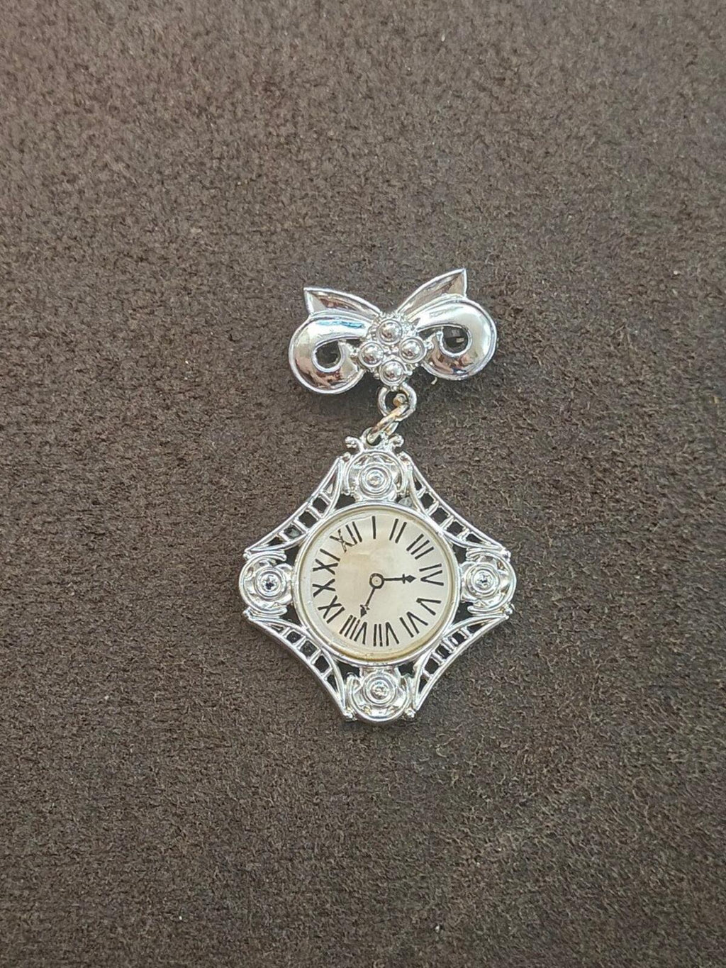 Silver-tone bow clock brooch, front view; filigree square frame with roman numeral clock.
