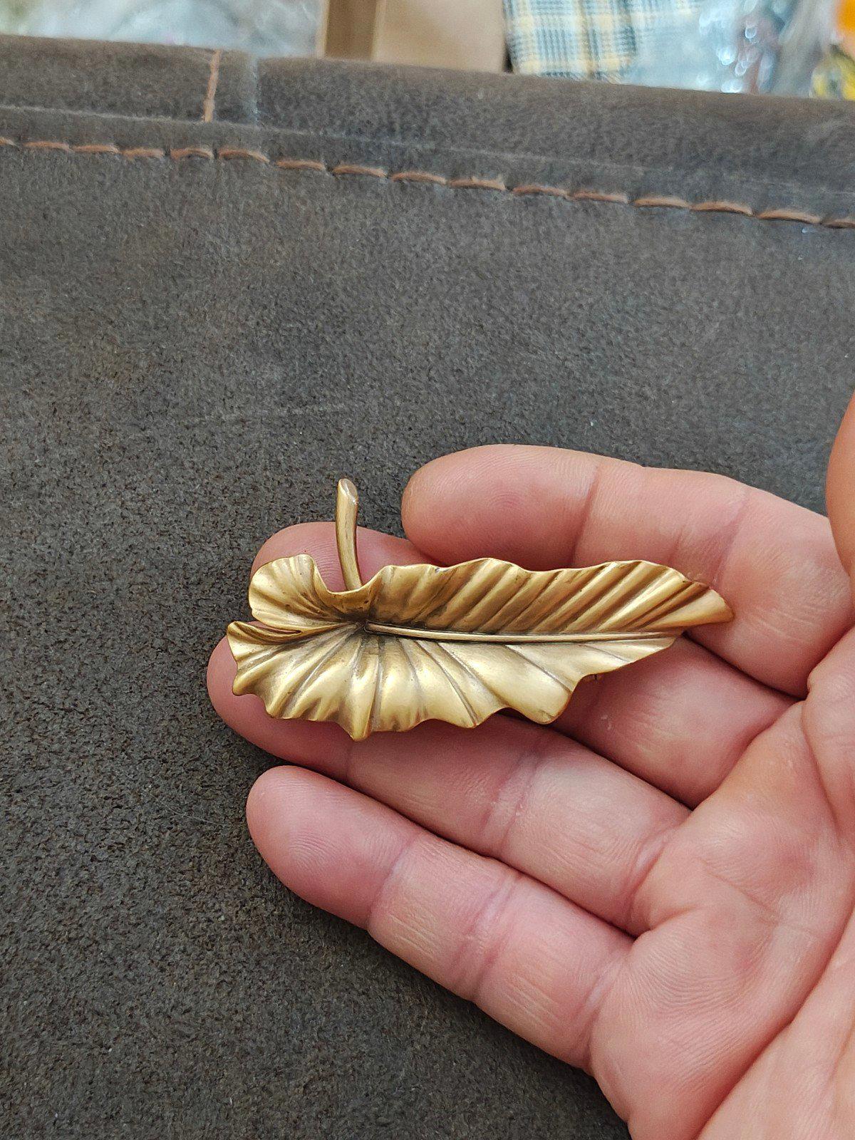 Gold-tone leaf brooch pin with ridged texture and small stick pin, held in hand.