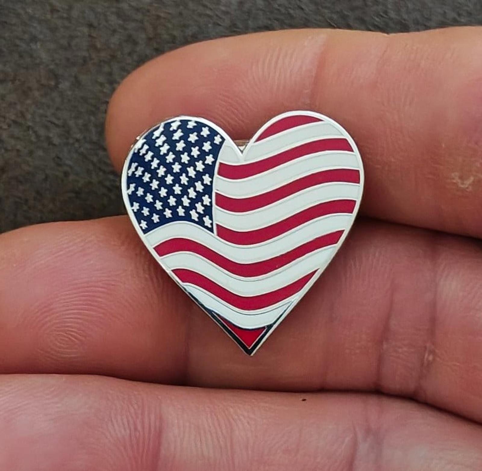 Heart-shaped enamel flag pin in hand, blue stars with red and white wavy stripes