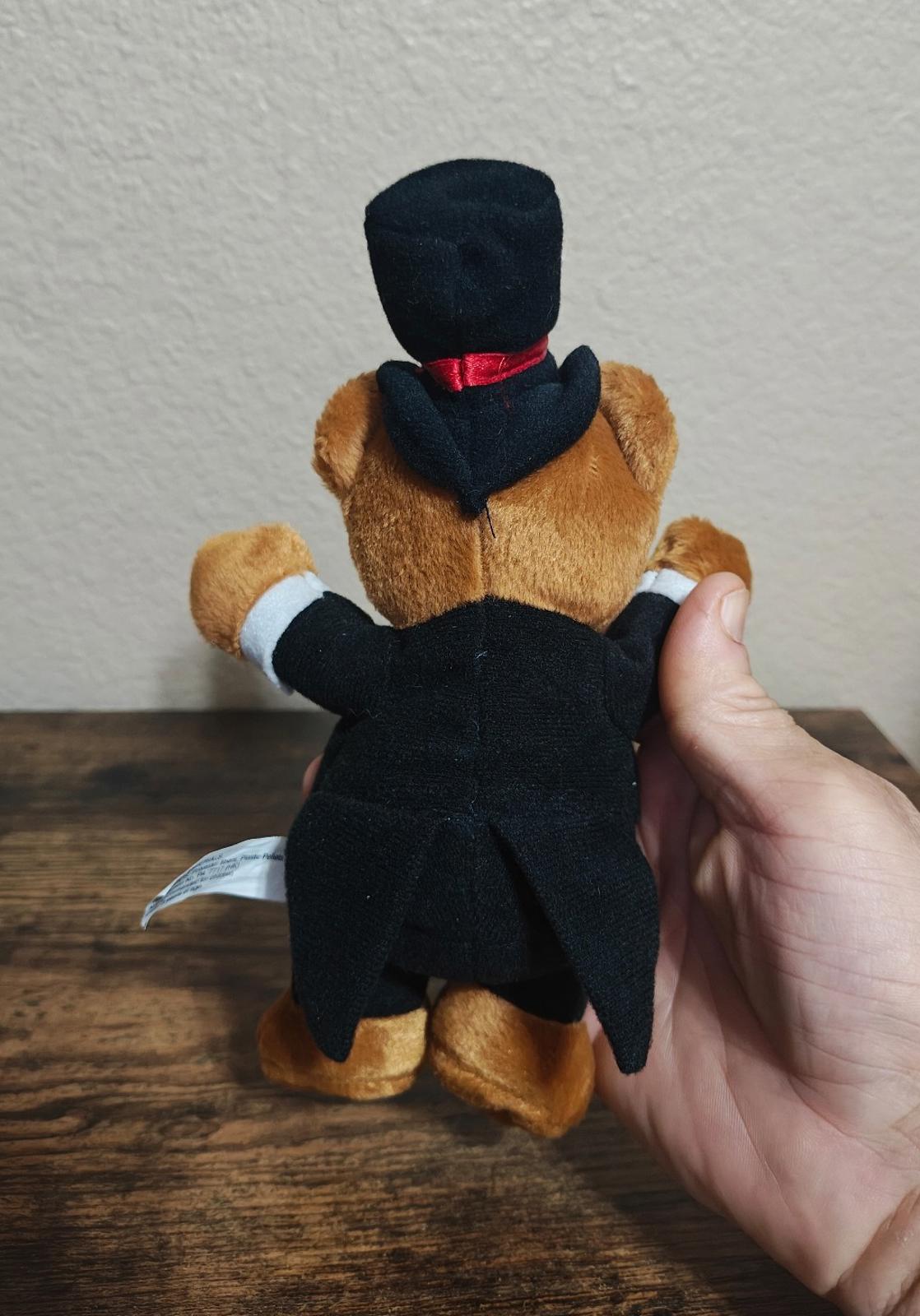 Back view plush bear in black tuxedo with white cuffs and tall top hat with red band.