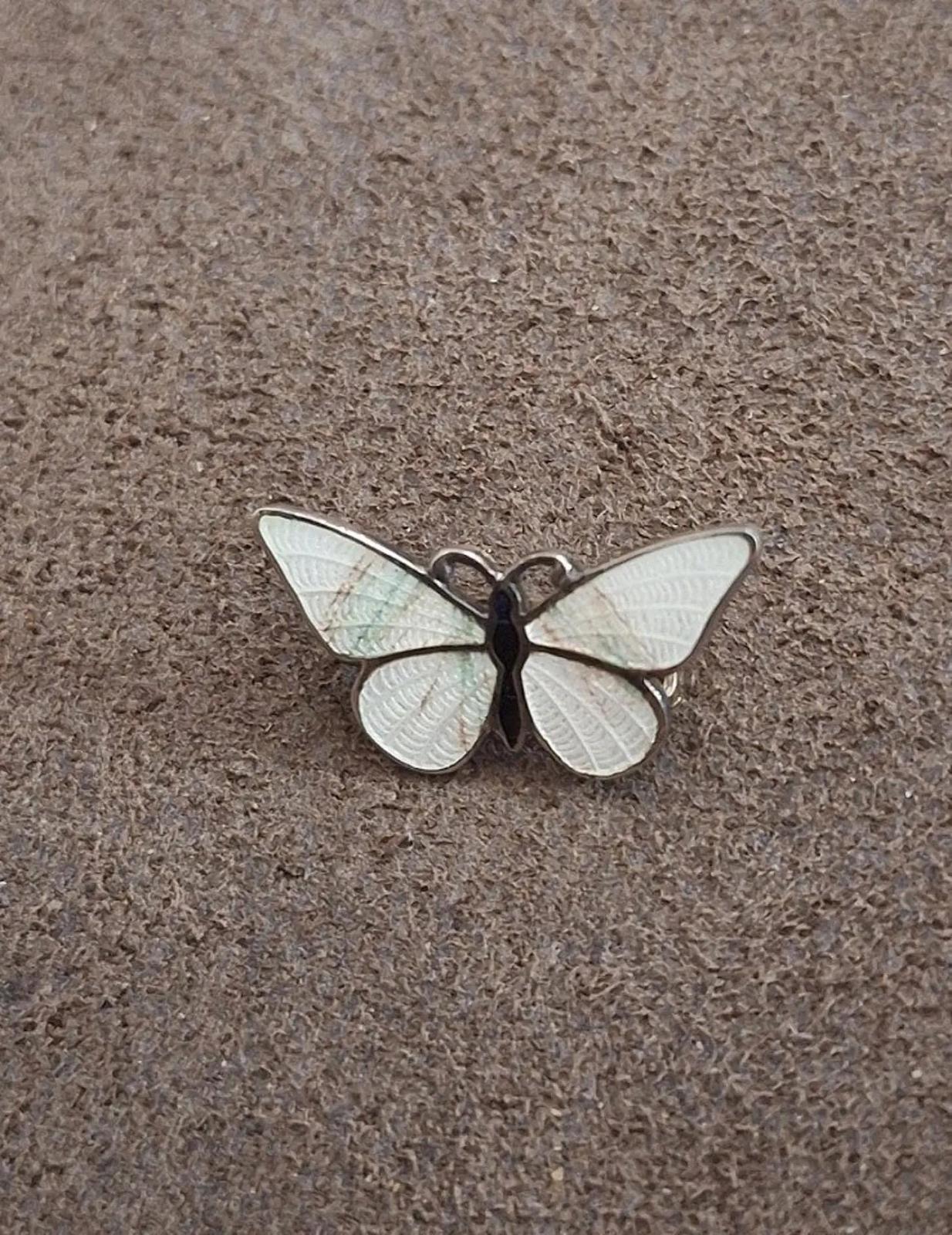 Enamel butterfly pin brooch with four white wings and dark body, laid on fabric.