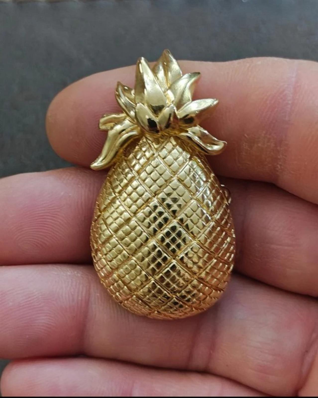 Gold tone pineapple brooch with leaf detail and textured body, held in hand