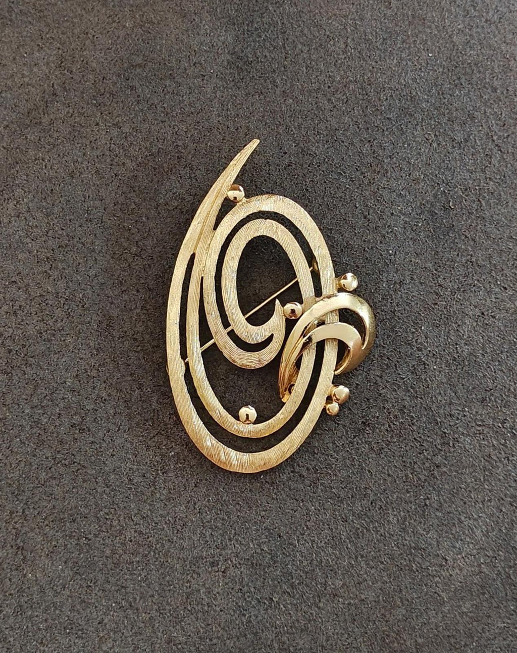 Gold tone oval brooch pin featuring double swirl engraving and small round accents