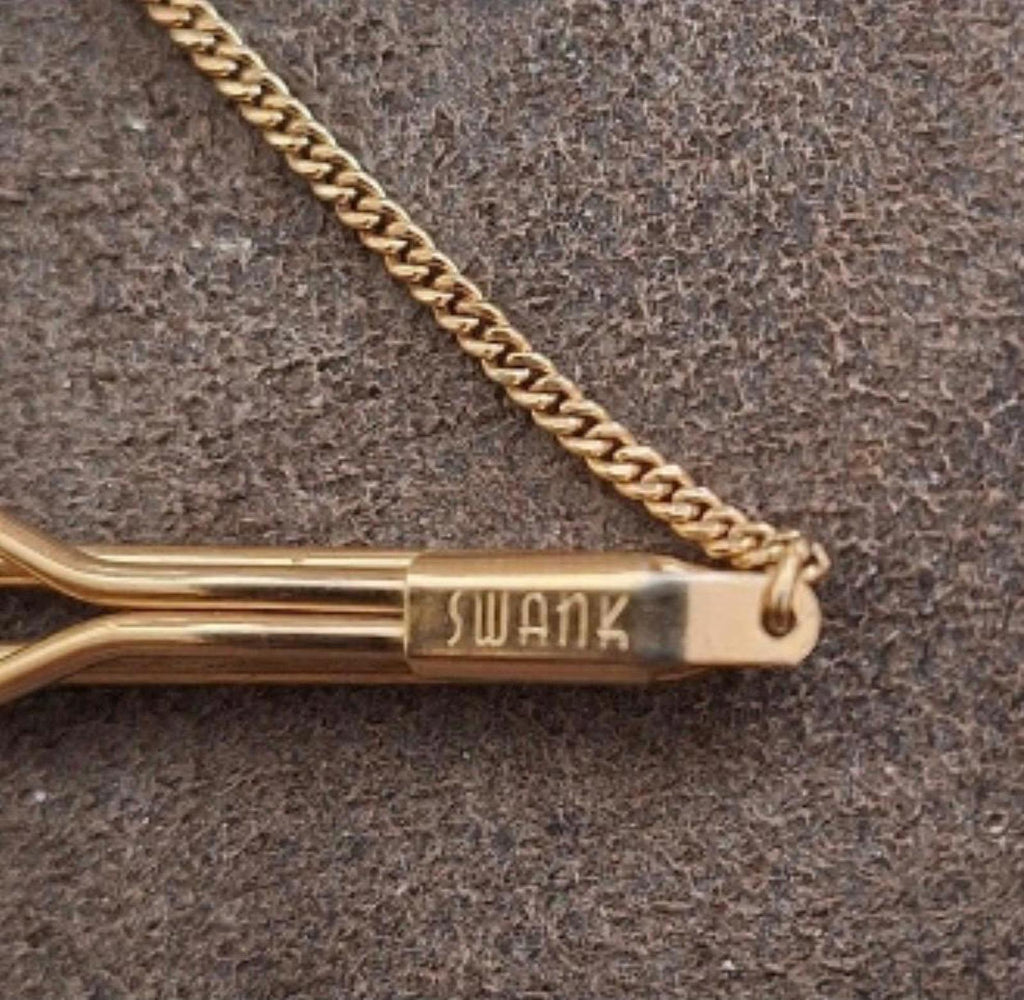 Close-up of gold-tone tie bar end with “SWANK” logo and connected chain.