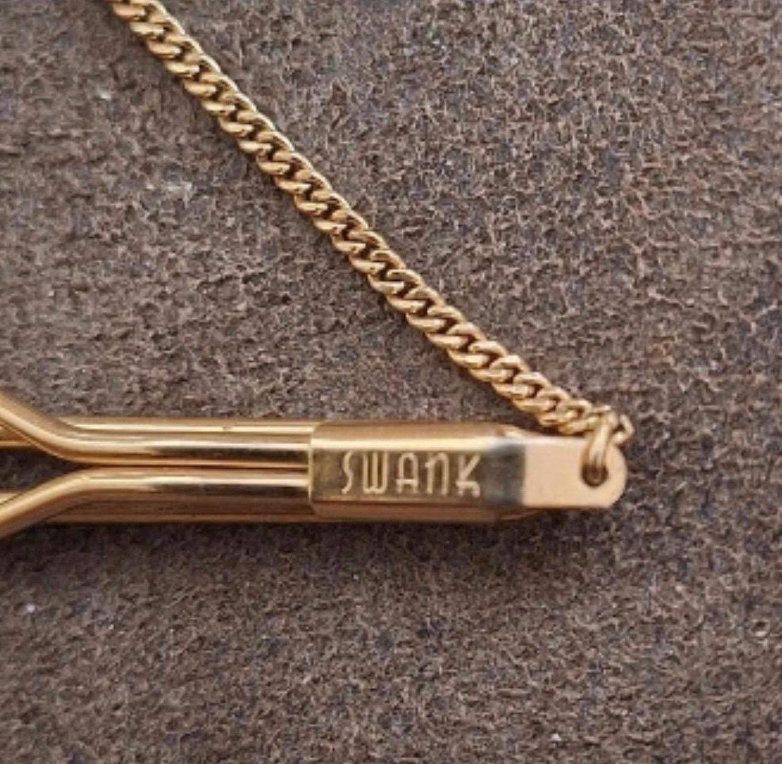 Close-up of gold-tone tie bar end with “SWANK” logo and connected chain.