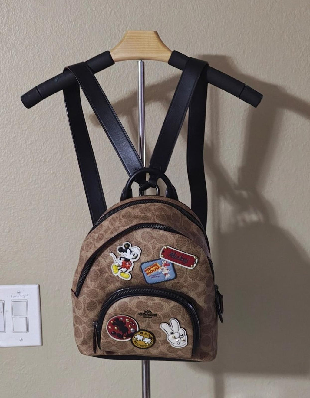 Brown signature canvas mini backpack with black straps, front patches, and top zipper