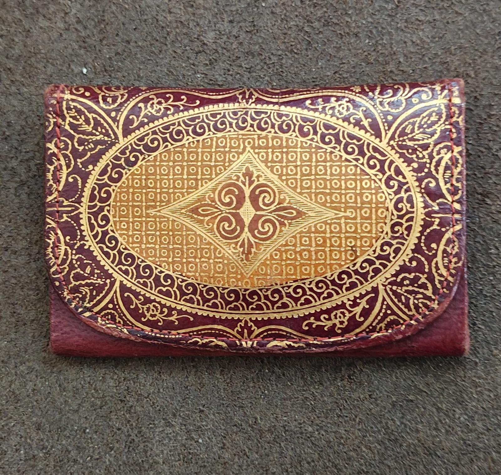 Front view of small coin purse wallet with burgundy leather and gold scrollwork pattern.