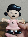 Bendable Lucy van Pelt figure in pink dress, black shoes, arms outstretched.