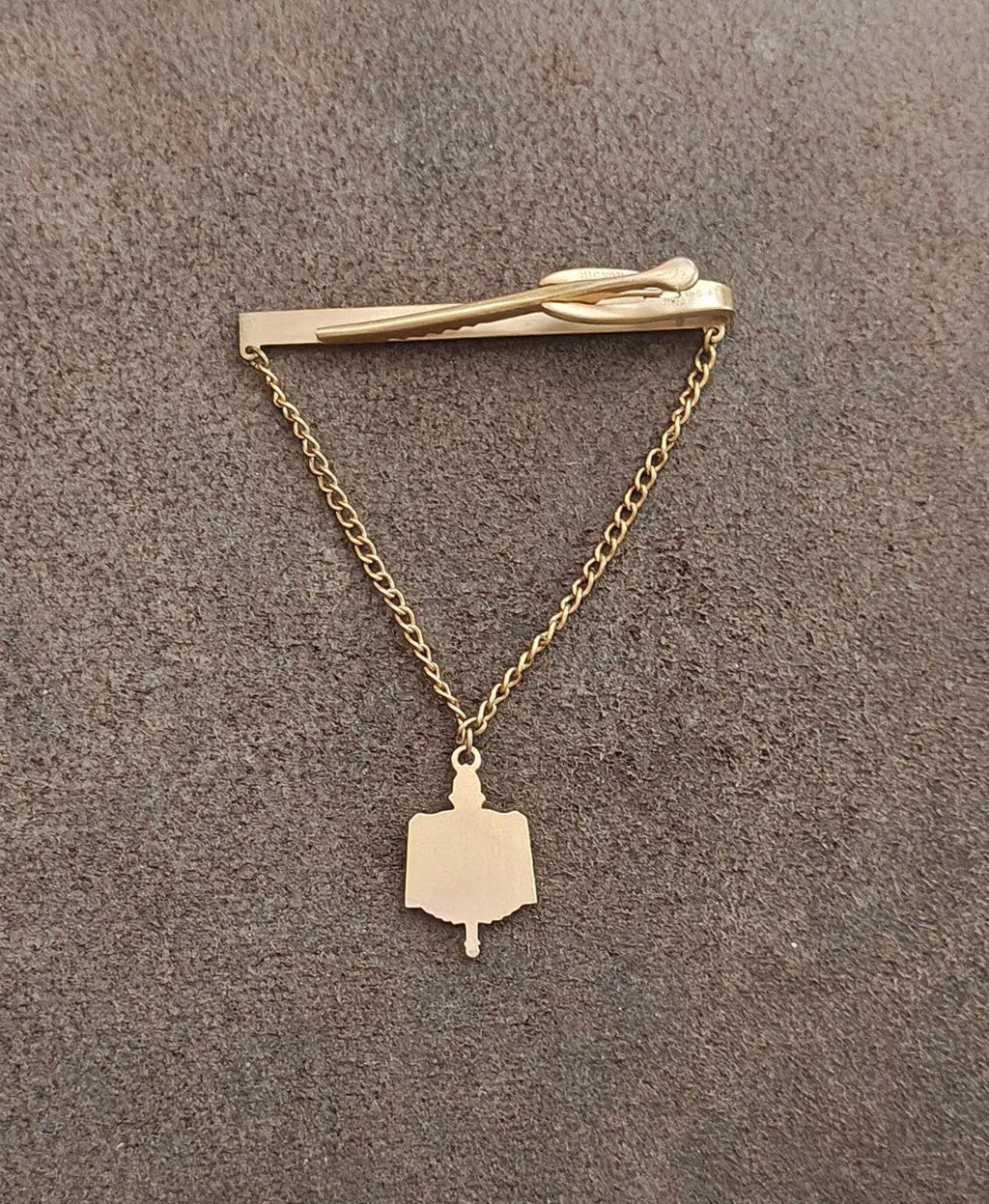 Gold-tone tie clip with chain and unmarked book-tag charm