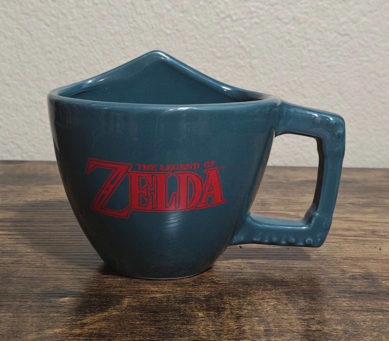Blue Zelda mug with red 'Zelda' logo and gray-blue handle, front angled view.