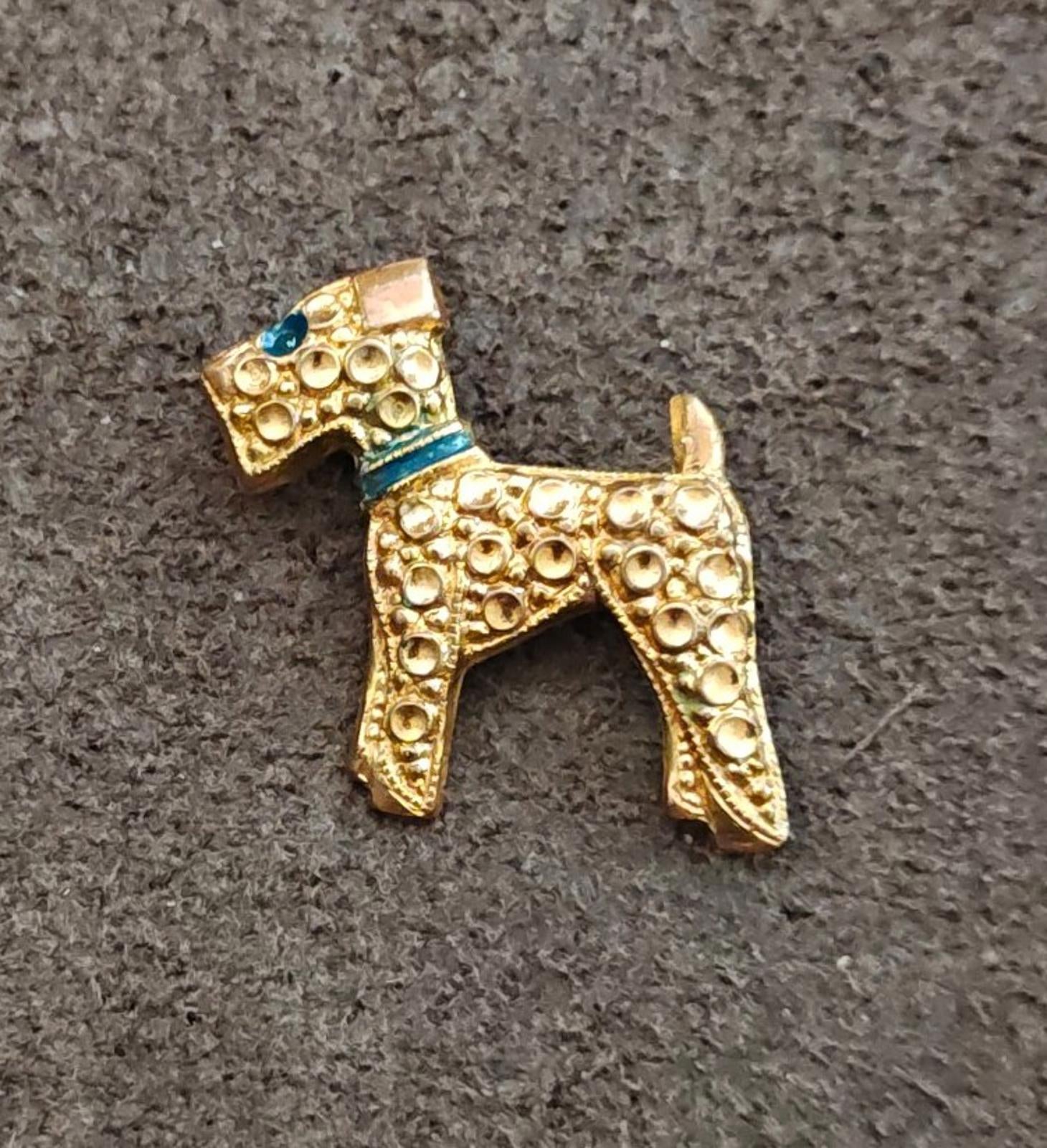 Gold-tone terrier dog brooch with blue enamel neck band and textured ornate finish.