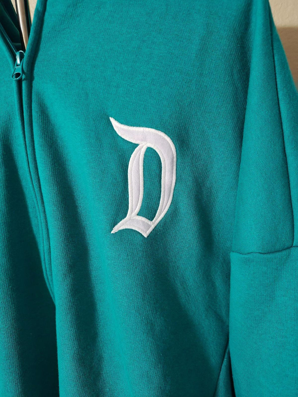 Teal hoodie with close-up of white letter D logo on chest