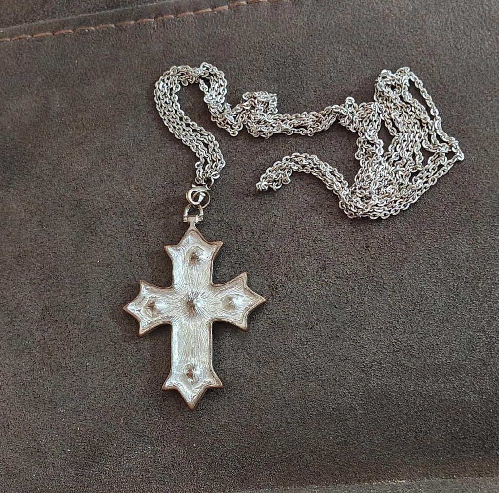 Silver tone cross pendant necklace with textured silver finish and small red stone details