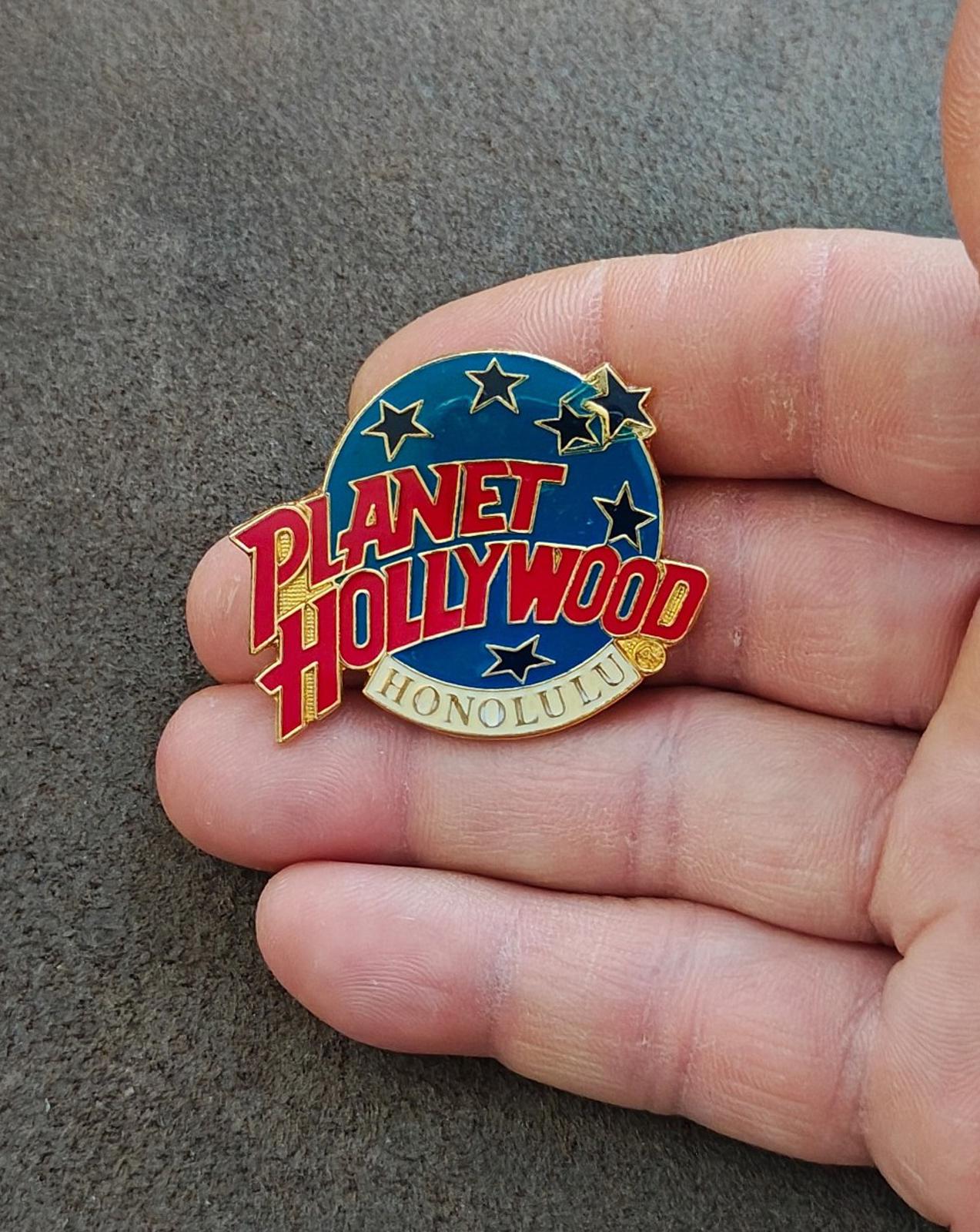 Planet Hollywood Honolulu enamel pin held in hand, side angle showing gold-tone edges