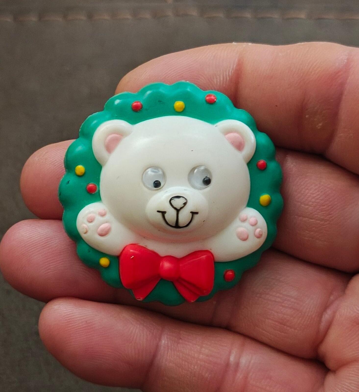 Green bear wreath pin with white face, googly eyes, red bow, and small dots