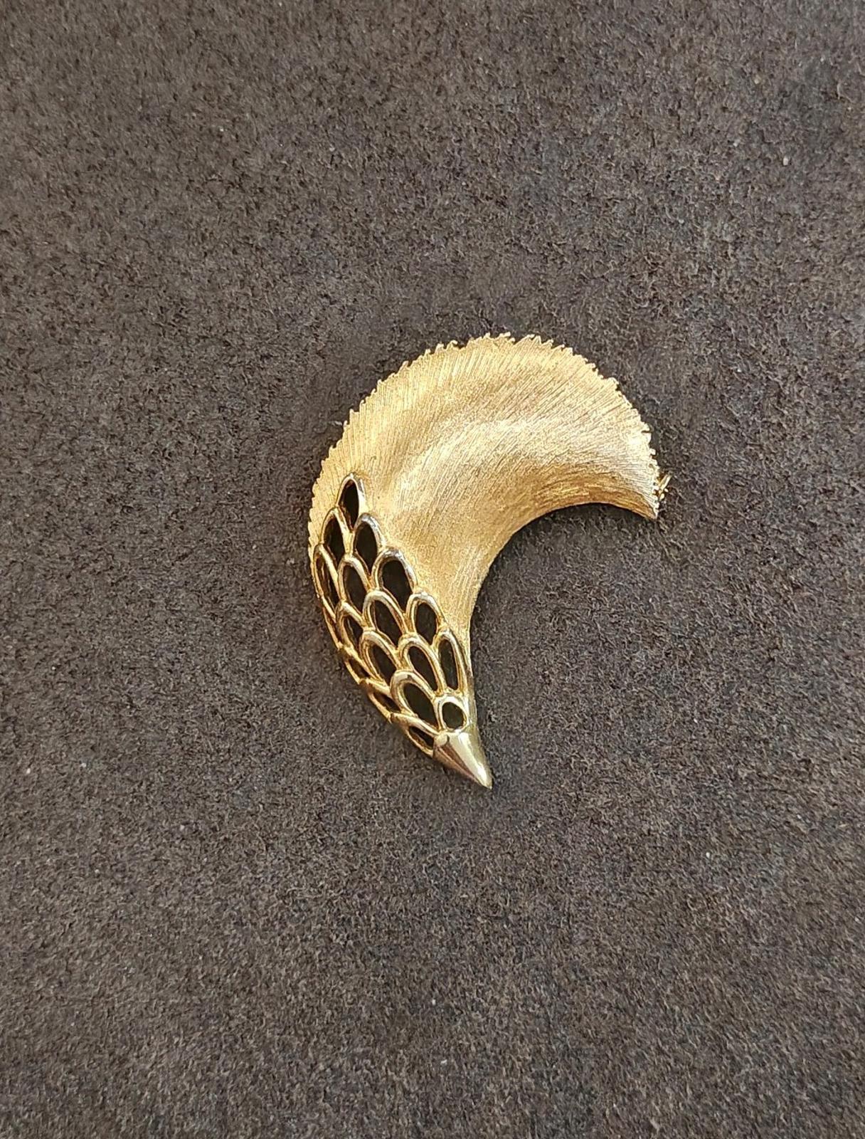Gold tone feather plume brooch on dark gray background, curved top and pointed tip