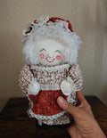 Handmade cloth doll canister with smiling face, white bonnet and red skirt, seated.