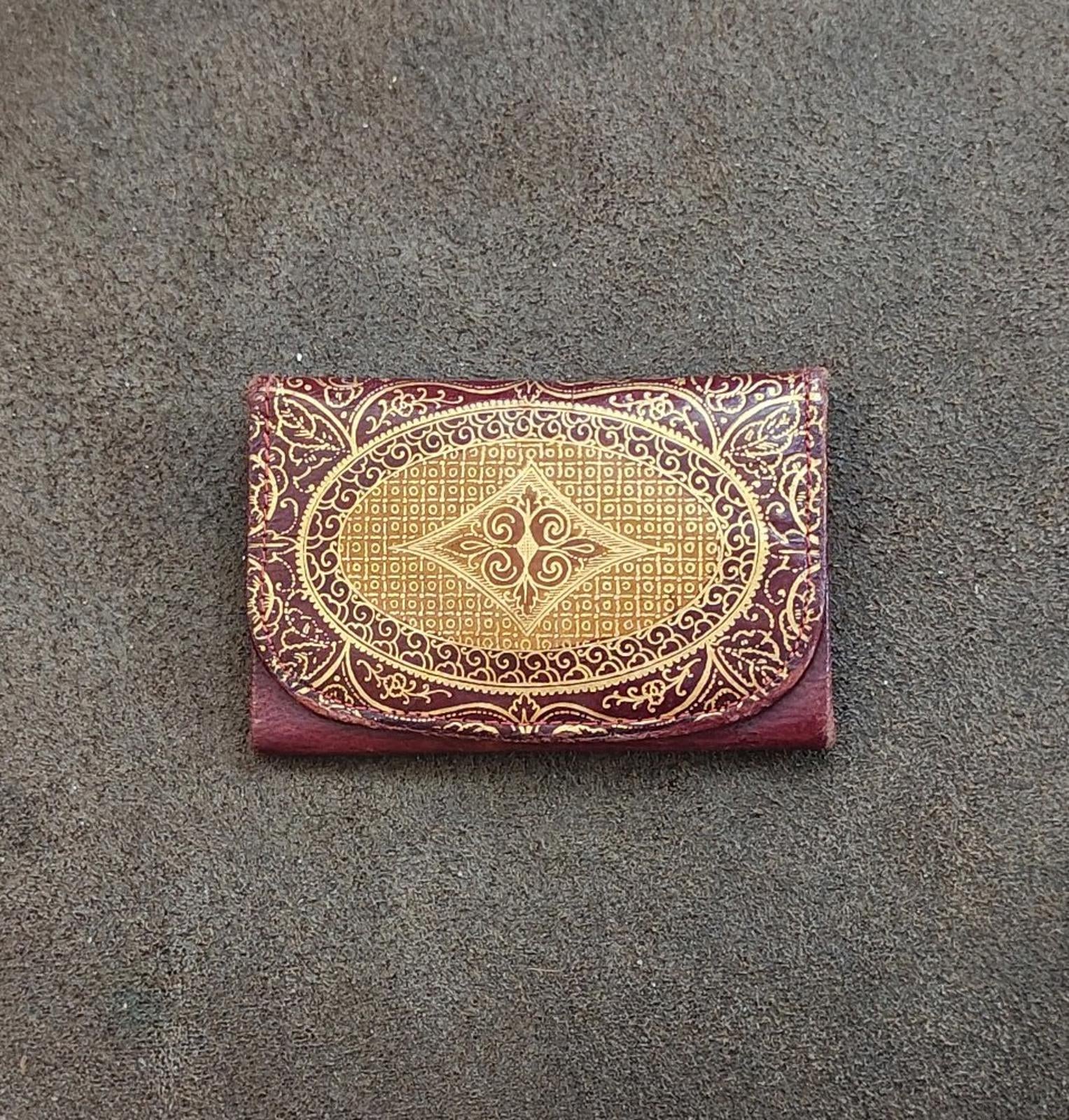 Burgundy small coin purse wallet with gold embossed ornate oval design on front.
