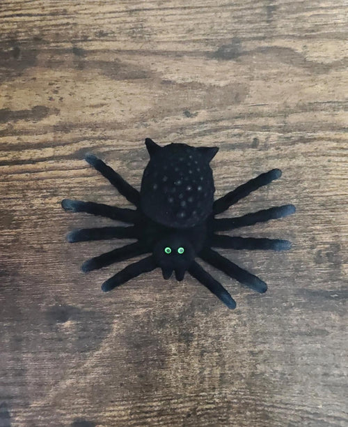 Black flocked spider figurine with green glowing eyes on a wooden surface.