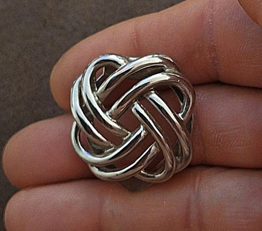 Silver love-knot scarf clip with interlocking knot design, close-up on hand
