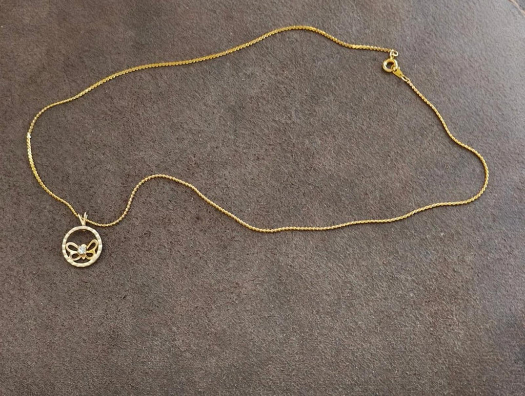 Gold-tone chain necklace with round butterfly pendant and small charm detail at clasp end