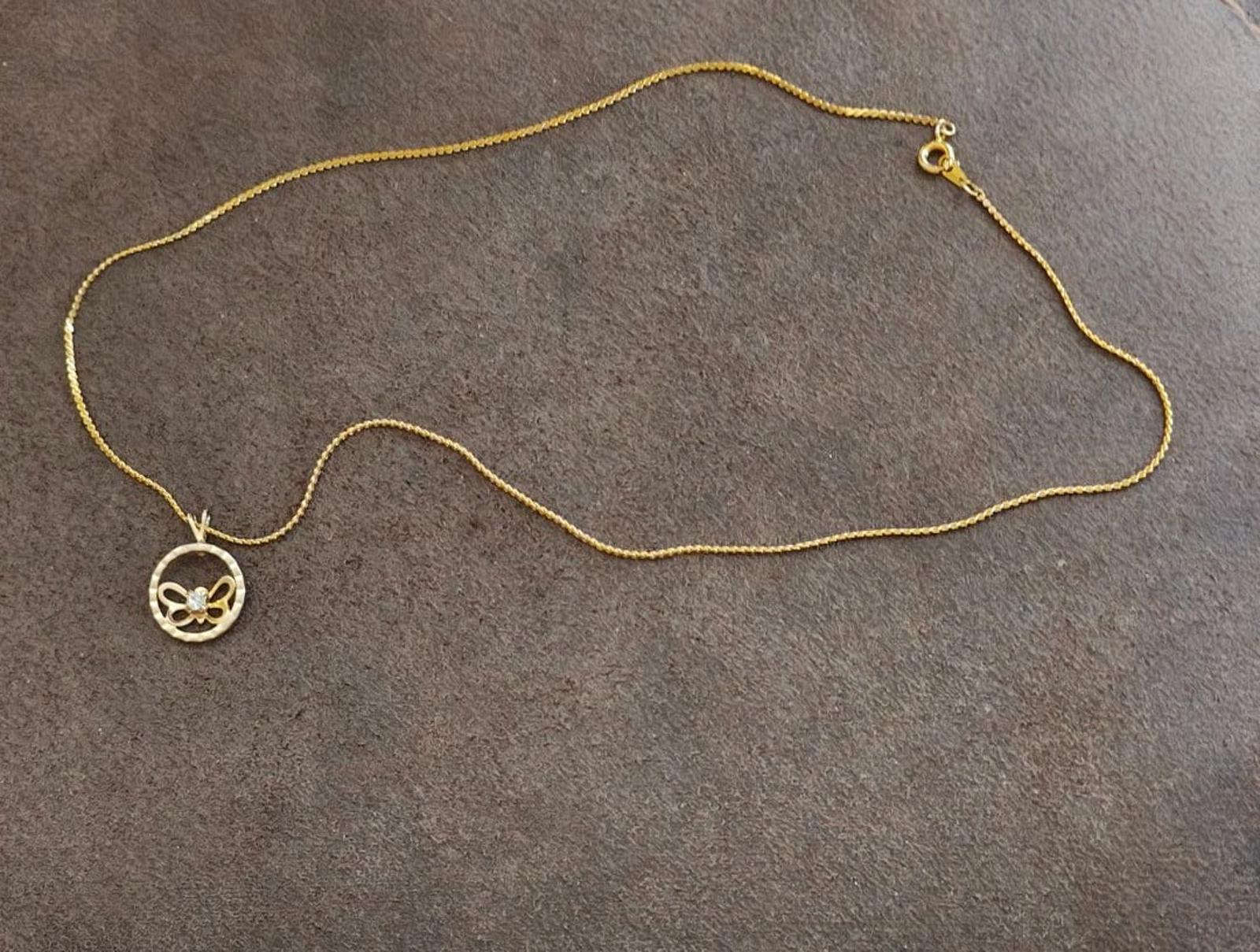 Gold-tone chain necklace with round butterfly pendant and small charm detail at clasp end