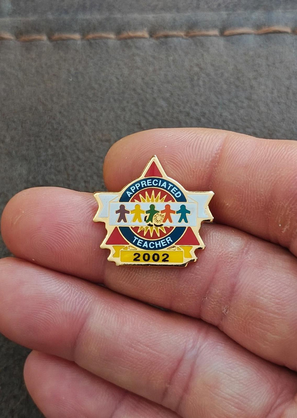 Small teacher enamel pin in hand with “Appreciated Teacher” and gold “2002”