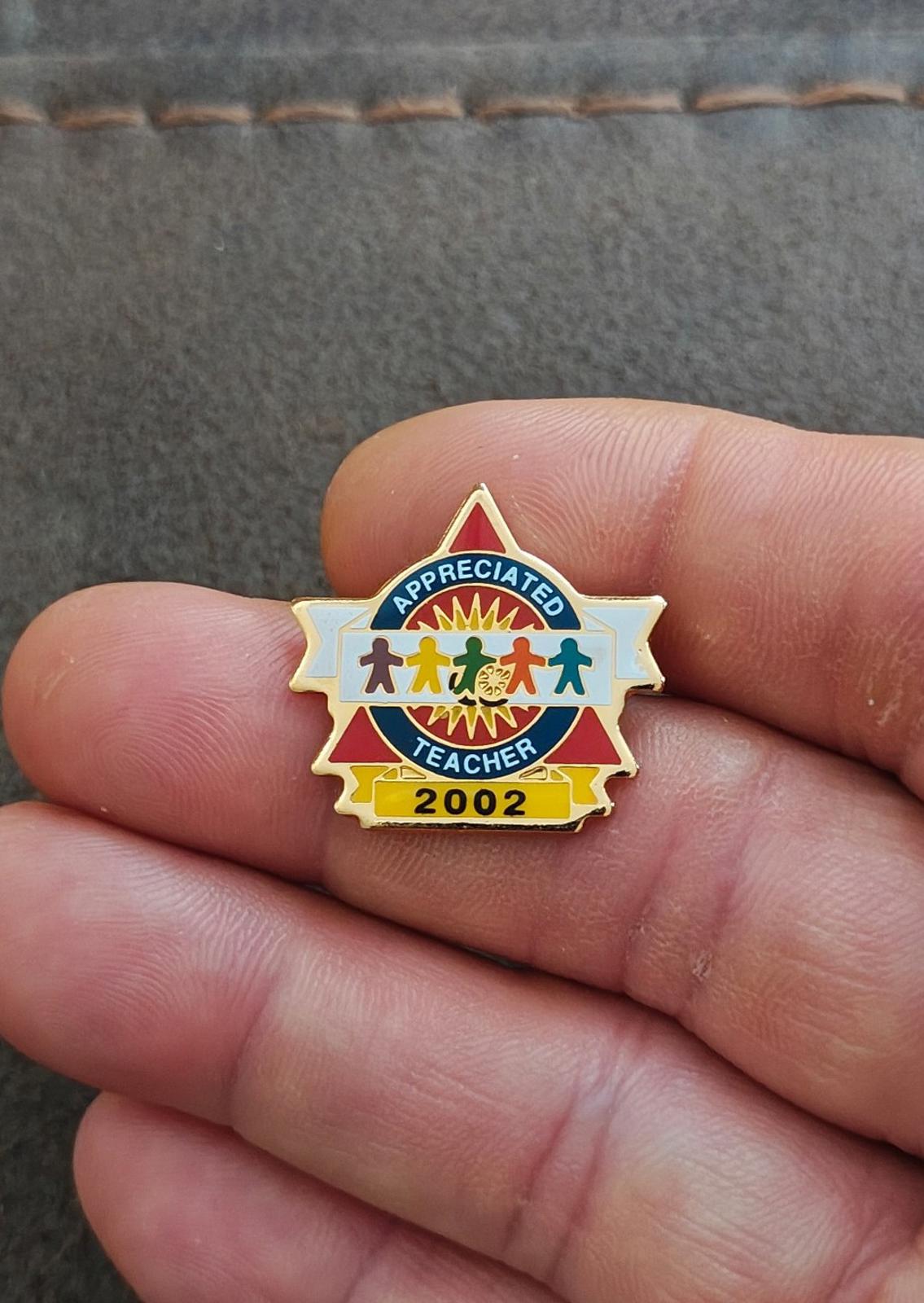 Small teacher enamel pin in hand with “Appreciated Teacher” and gold “2002”