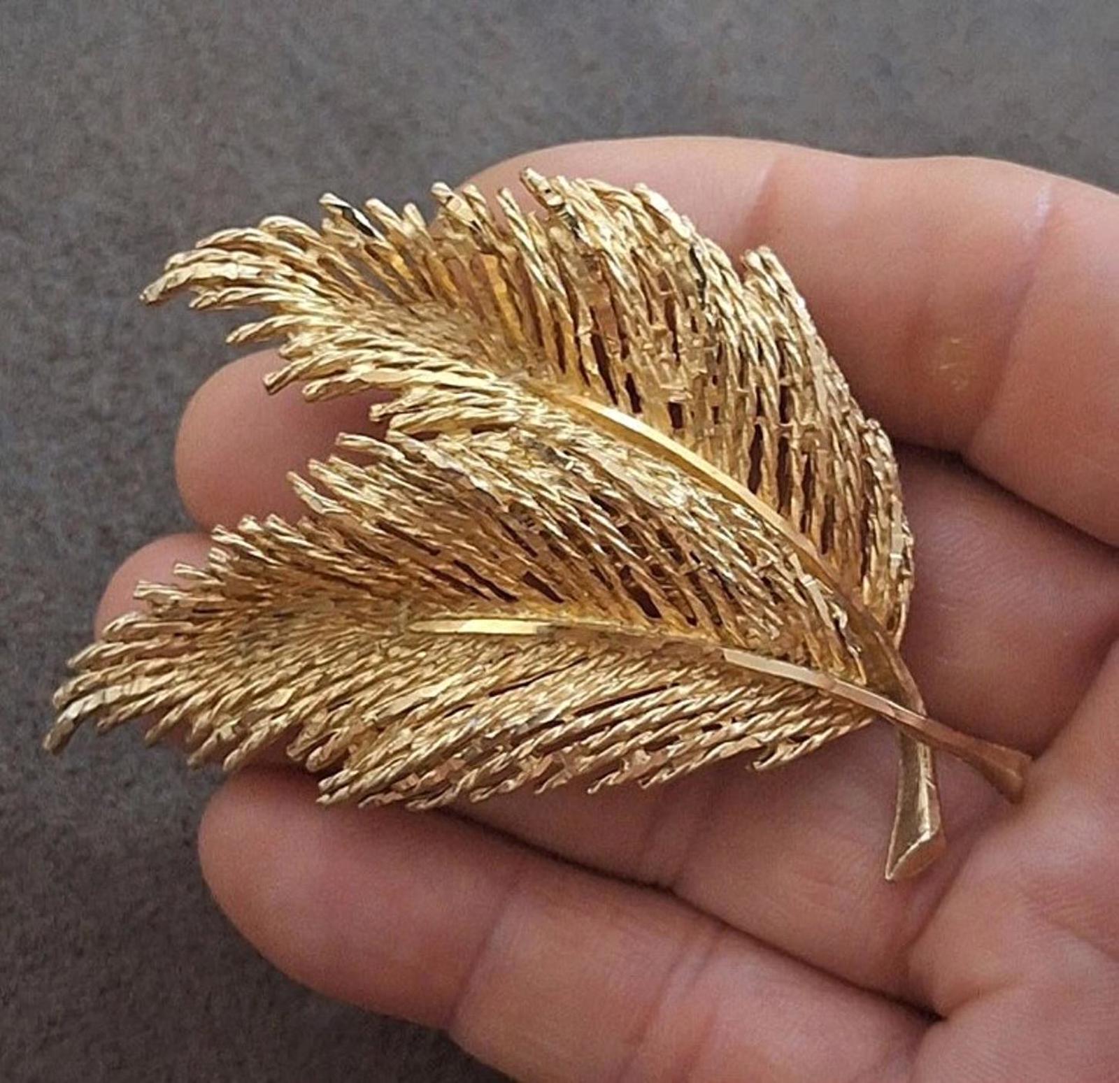 Gold-tone feather leaf pin brooch with two layered leaf shapes, held in hand