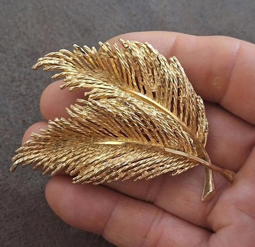Gold-tone feather leaf pin brooch with two layered leaf shapes, held in hand