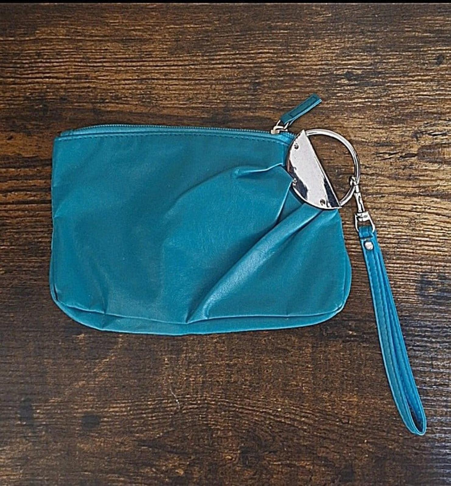 Teal clutch purse with zipper closure and wrist strap, side view on tabletop